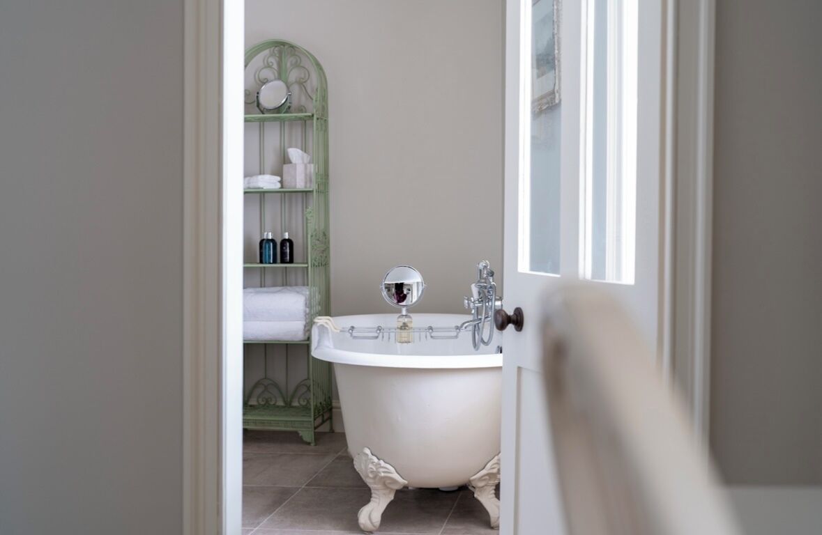 Une salle de bain avec une baignoire sur pieds, un meuble-lavabo vert doté d’étagères et un miroir.