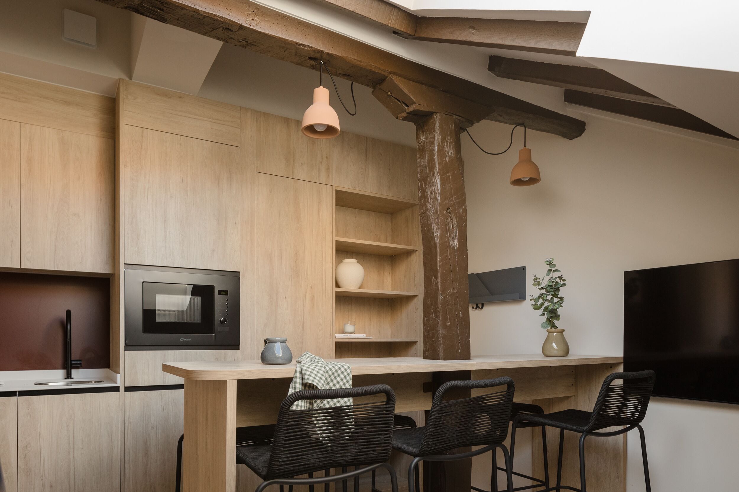 Eine moderne Küche mit Holzausbau, einer eingebauten Mikrowelle und einer Bar mit schwarzen Stühlen.
