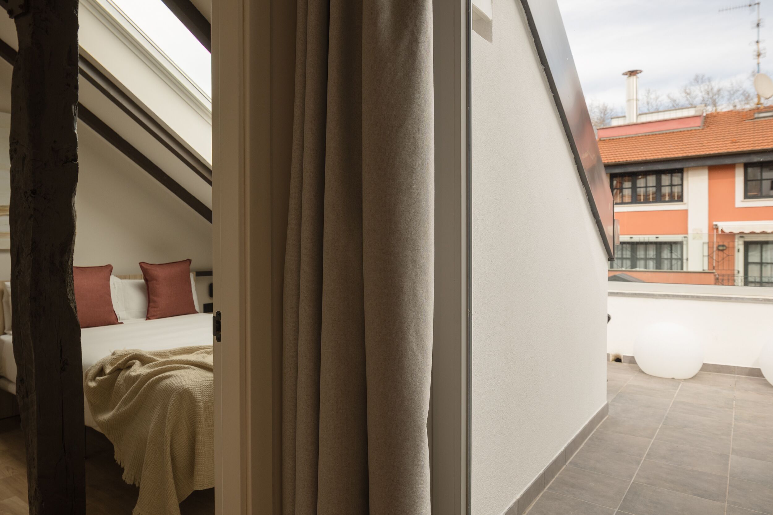 Un dormitorio con cama, almohadas y ventana con vista a un balcón.