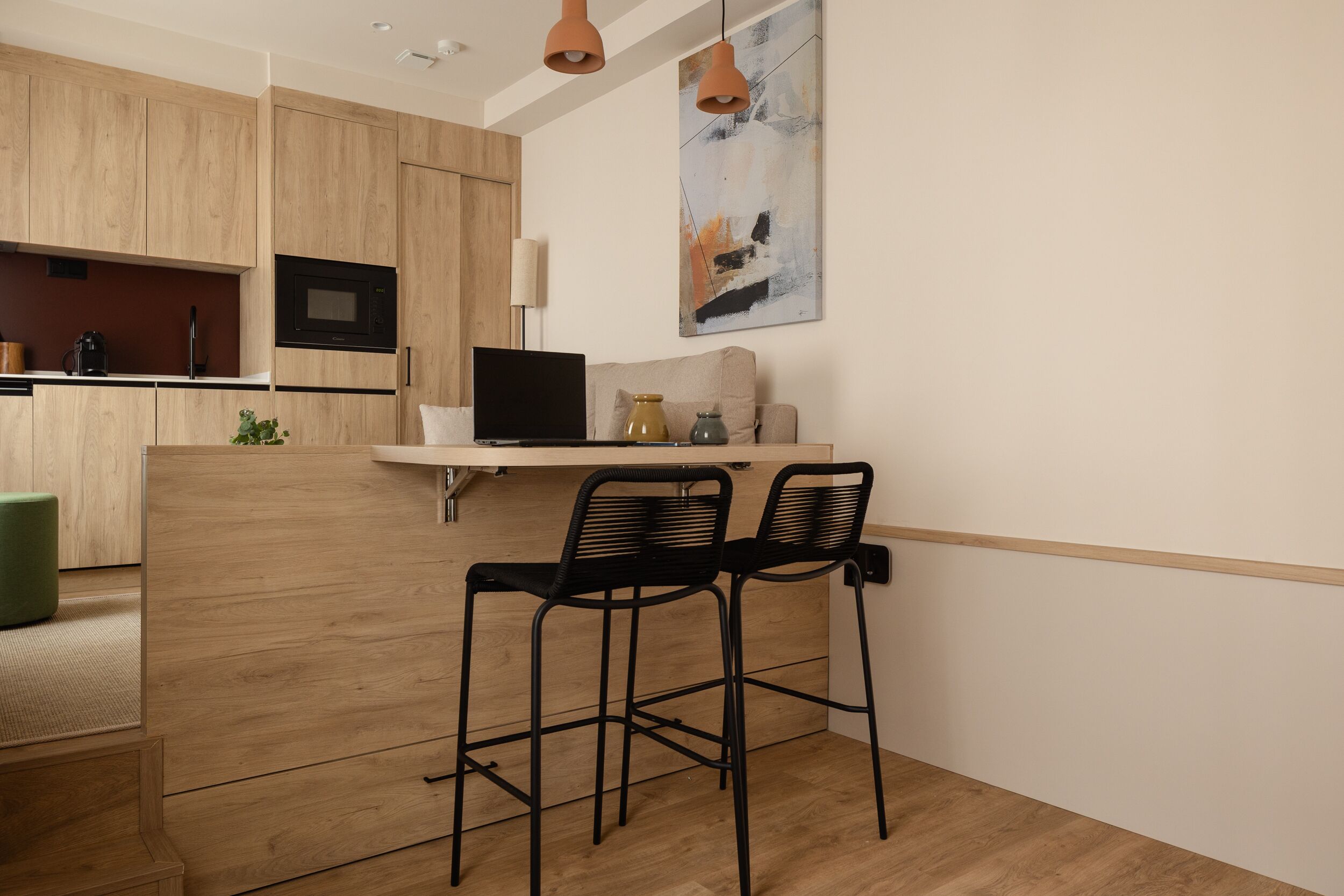 A modern kitchen with wooden cabinets, a built-in microwave, and a small dining area with two black chairs.