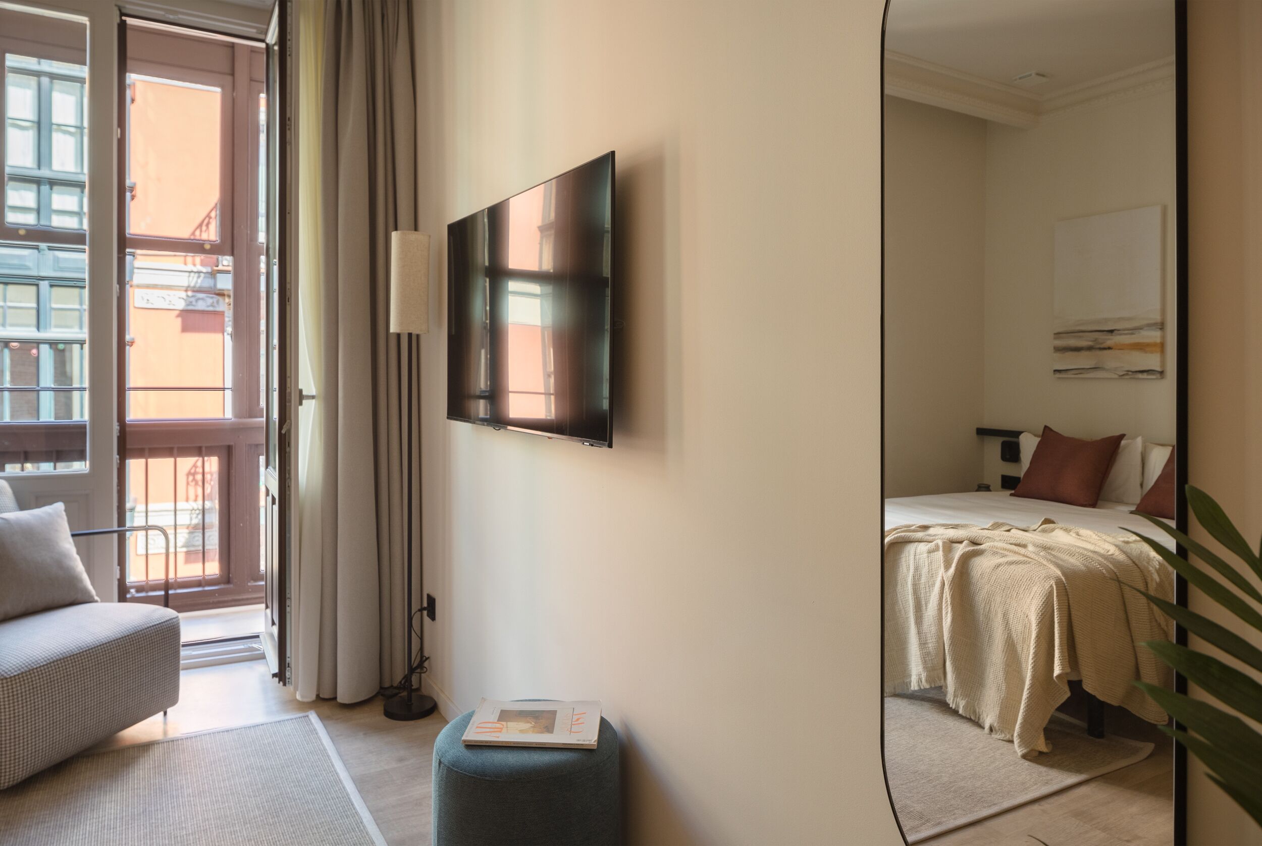 Ein Hotelzimmer mit Bett, einer Couch, einem Flachbildfernseher an der Wand, einem kleinen Tisch und einem Fenster mit Vorhängen.