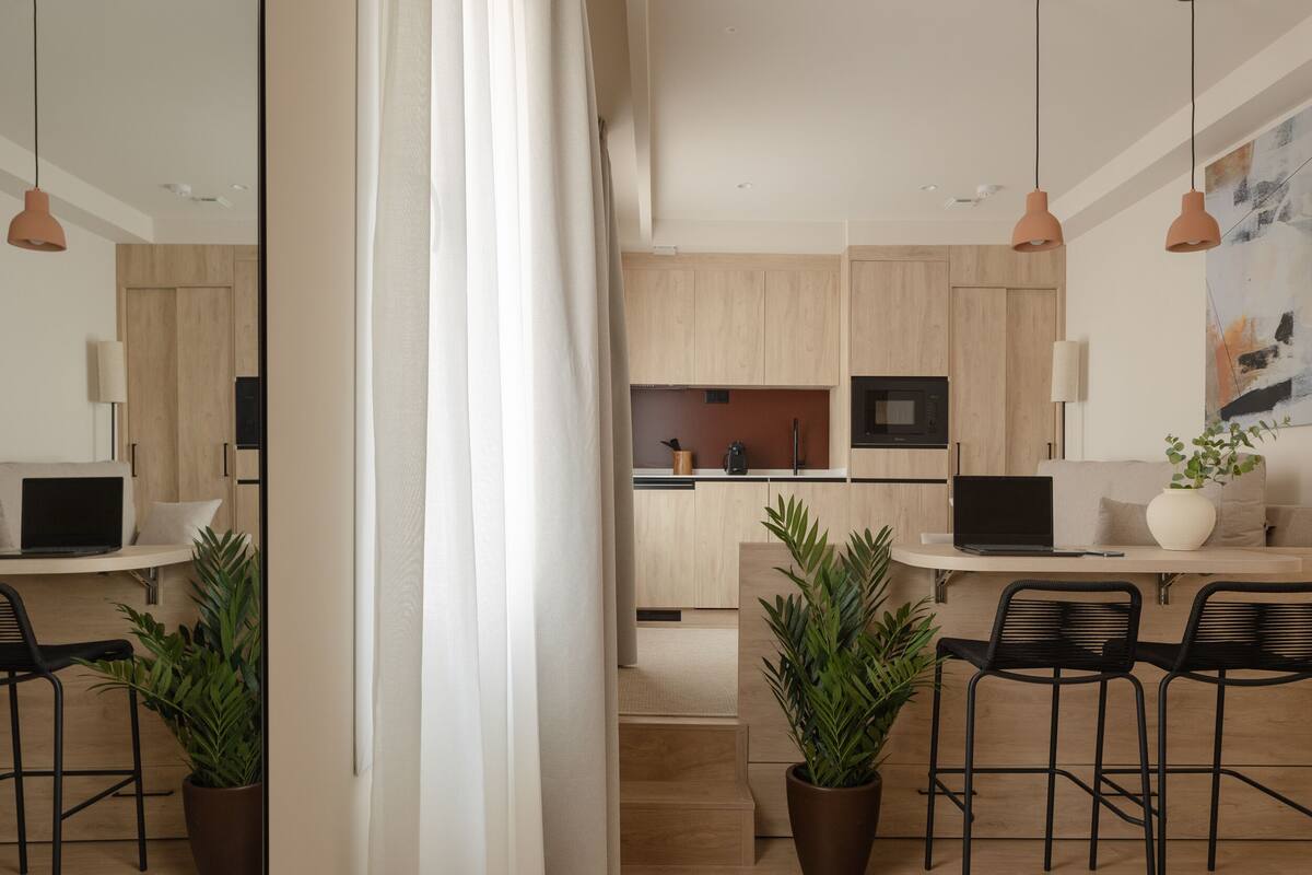 A modern kitchen with wooden cabinets, a central island, and a dining area with two black chairs and a table.