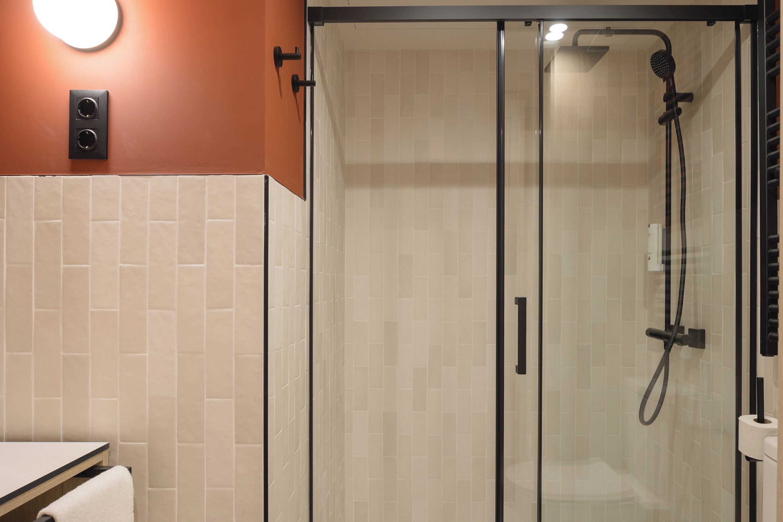 Une douche fermée par des parois en verre, dotée d’un pommeau de douche à main et d’un robinet mural.