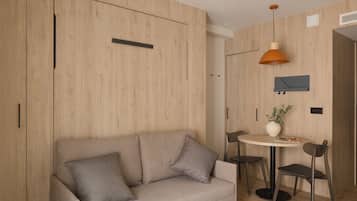 A modern room with a wooden wardrobe, a sofa with cushions, a round table with chairs, and a hanging pendant light.