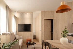 Una sala de estar moderna con sofá, televisor montado en la pared, mesa de comedor con sillas y una lámpara colgante naranja grande.