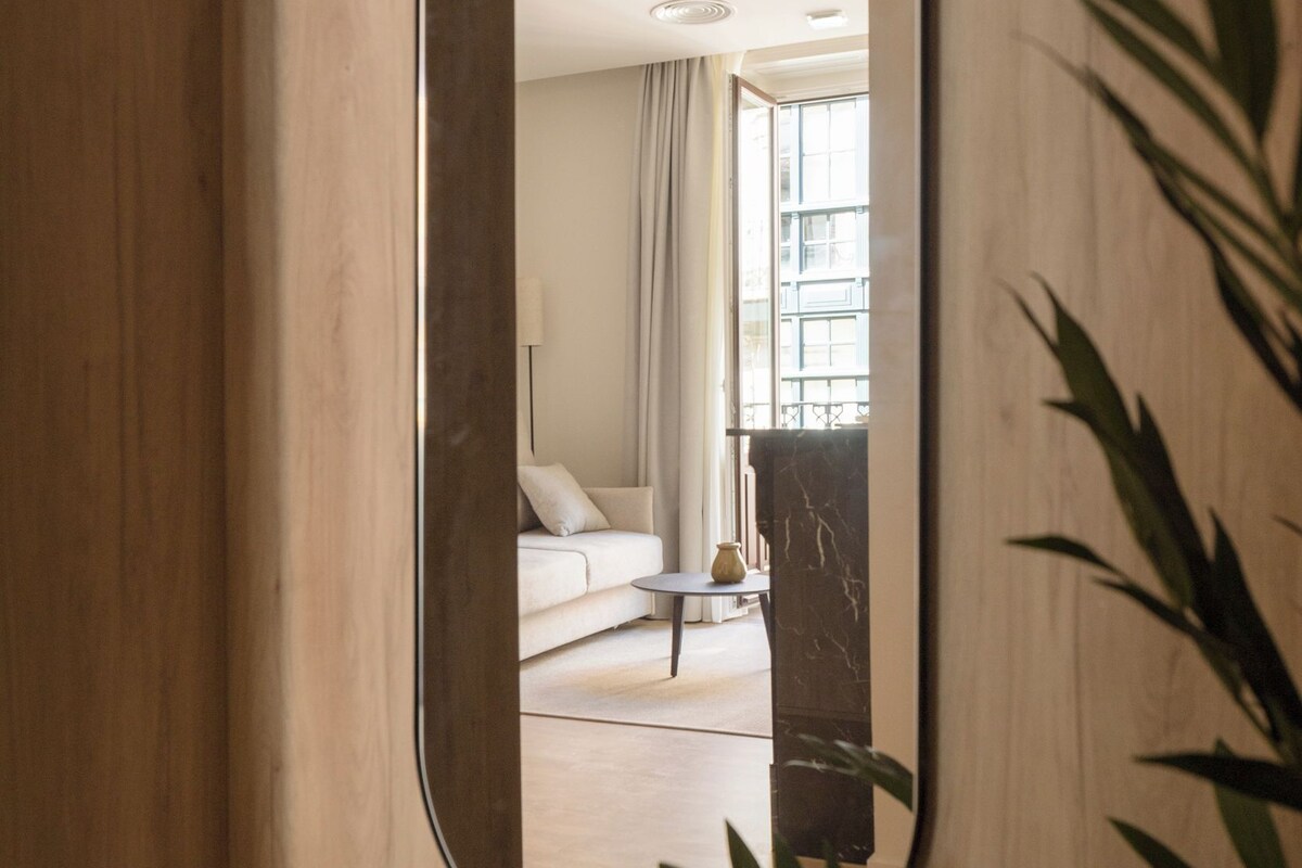 A mirror reflecting a room with a sofa, a small table, and a plant.