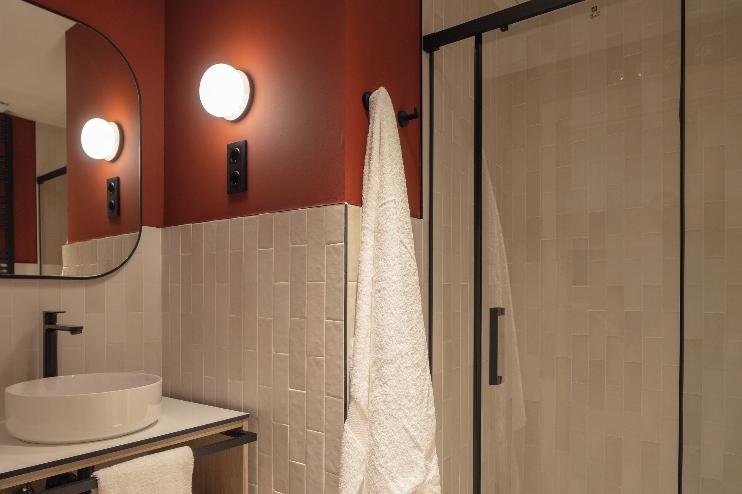 Un baño con un lavabo redondo, un espejo con iluminación y un perchero para toallas.