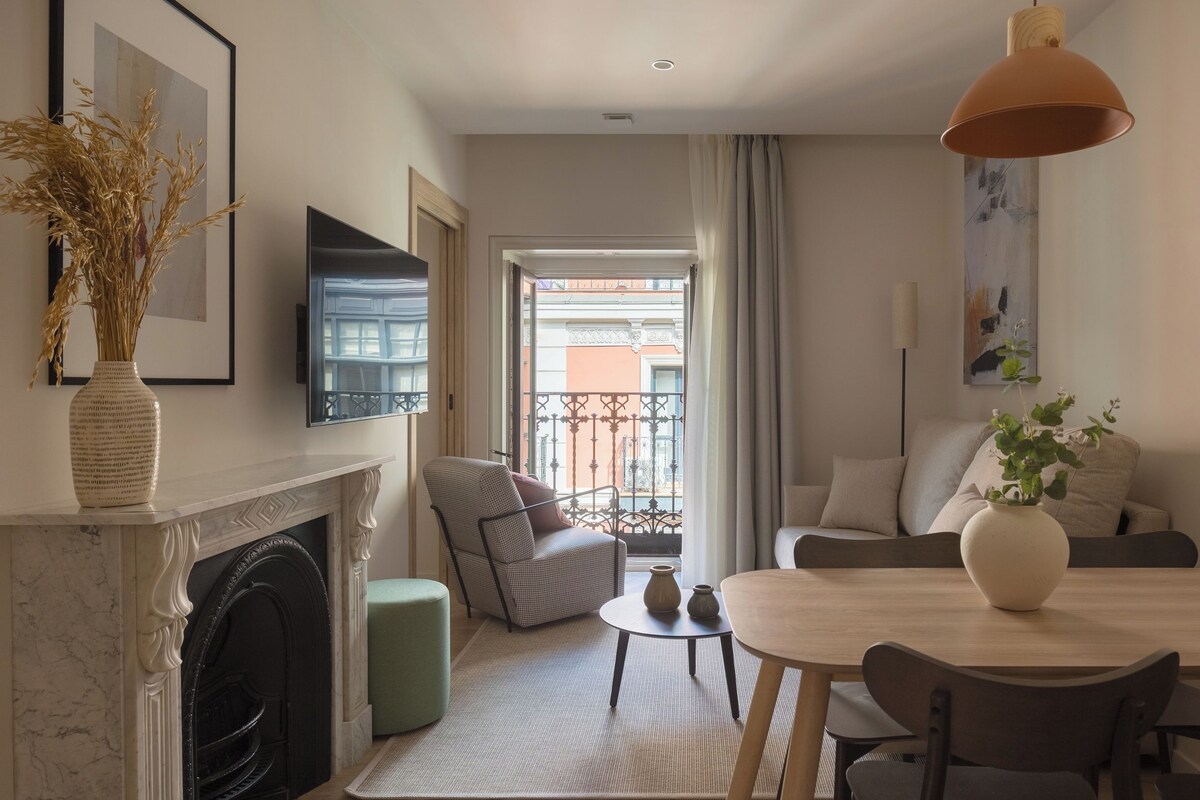 A modern living room with a fireplace, a sofa, a dining table, and a view of the outside balcony.