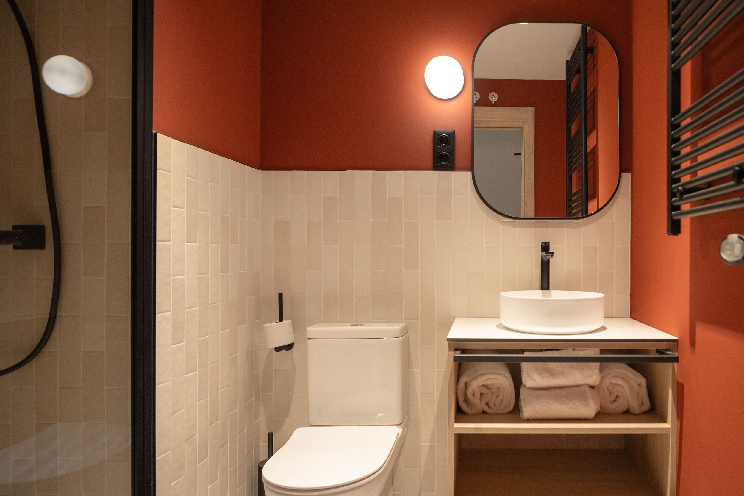 Baño con inodoro blanco, lavabo y espejo. Hay toallas en un estante.