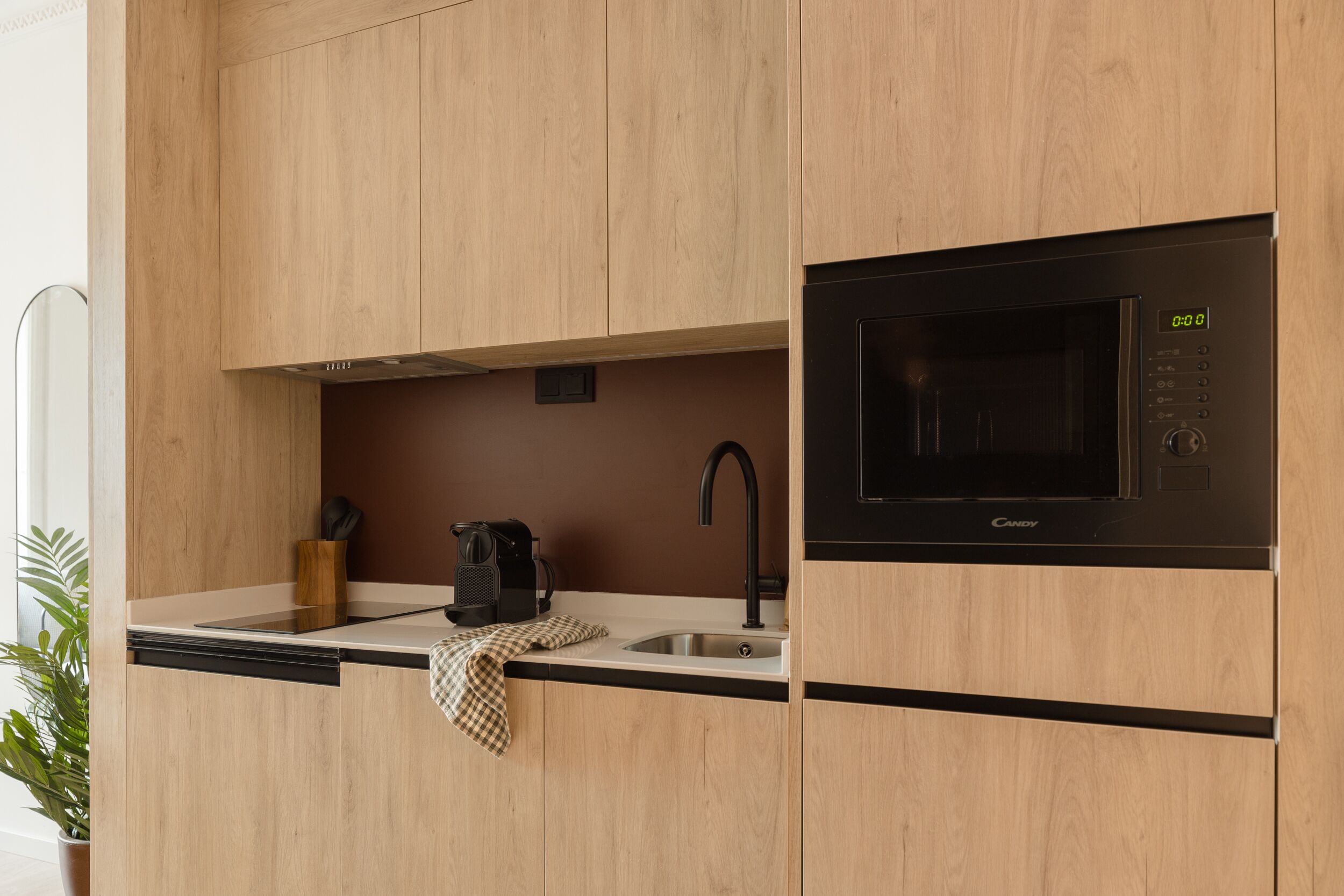 A modern kitchen with wooden cabinets, a built-in microwave, a sink, and a coffee maker.