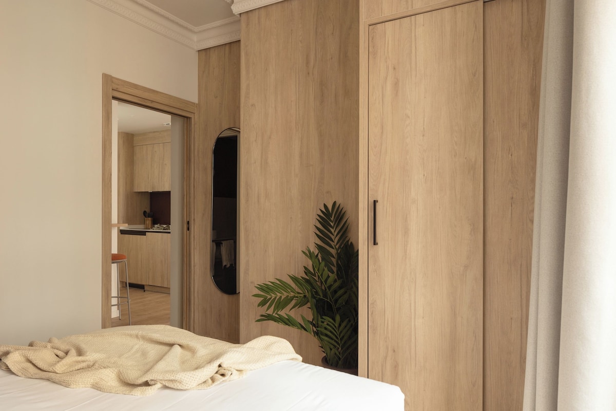 Un dormitorio con cama, armario de madera, espejo y planta en maceta.