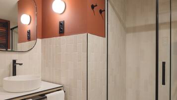 A bathroom with a round sink, a mirror, and a shower area.