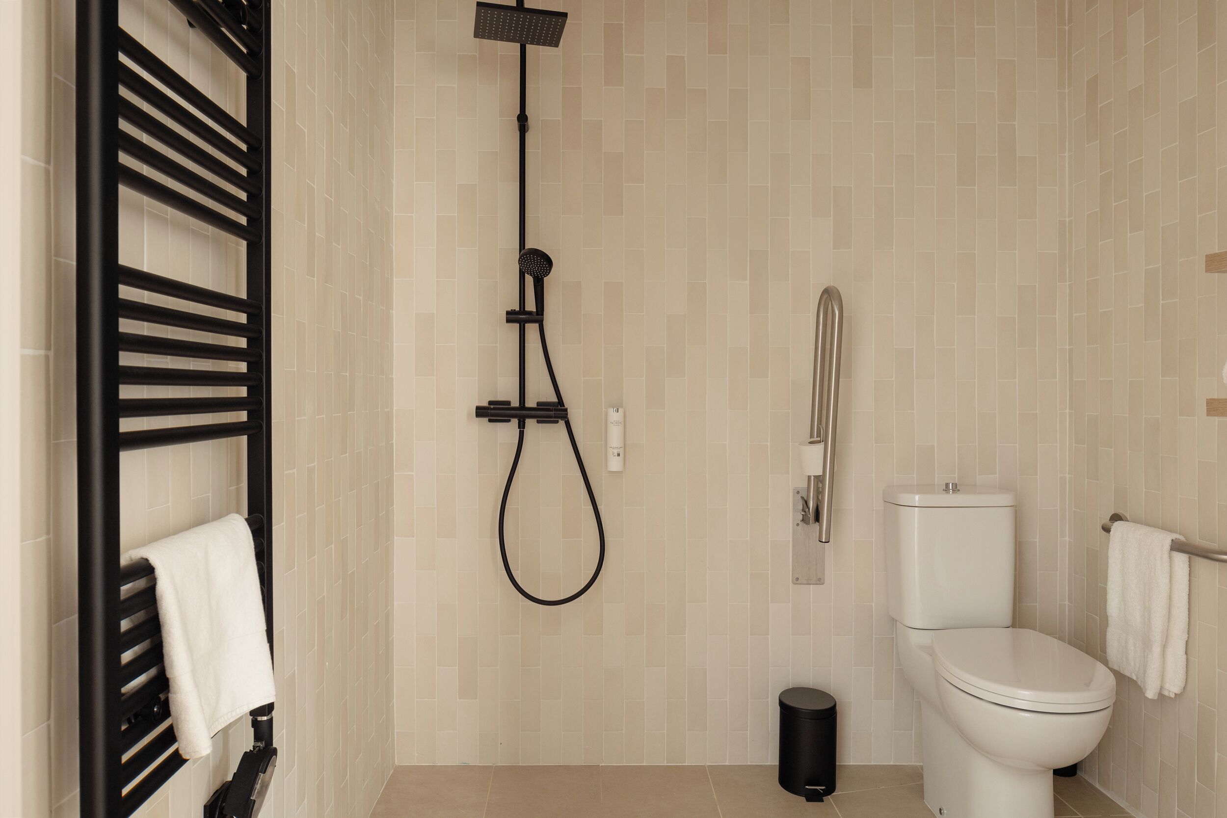 Un baño moderno con un toallero negro, un cabezal de ducha, un inodoro y un cubo de basura.