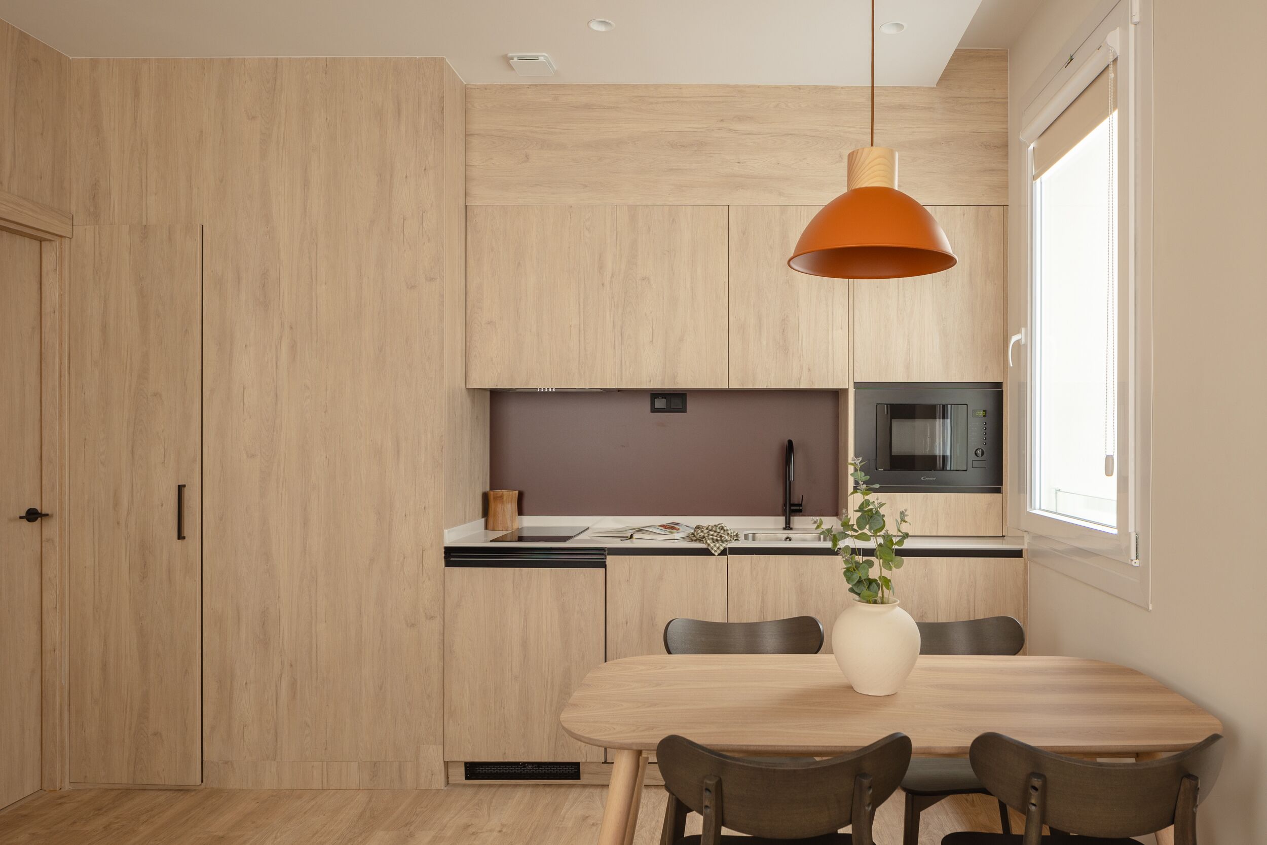 Une cuisine moderne avec des meubles en bois, un four à micro-ondes encastré et un coin repas comprenant une table et des chaises.
