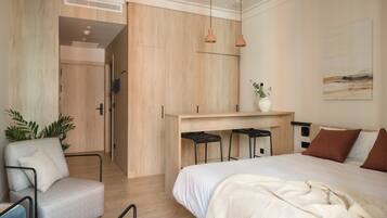 Een moderne slaapkamer met een groot bed, een bureau met twee krukken, een stoel en een plant.