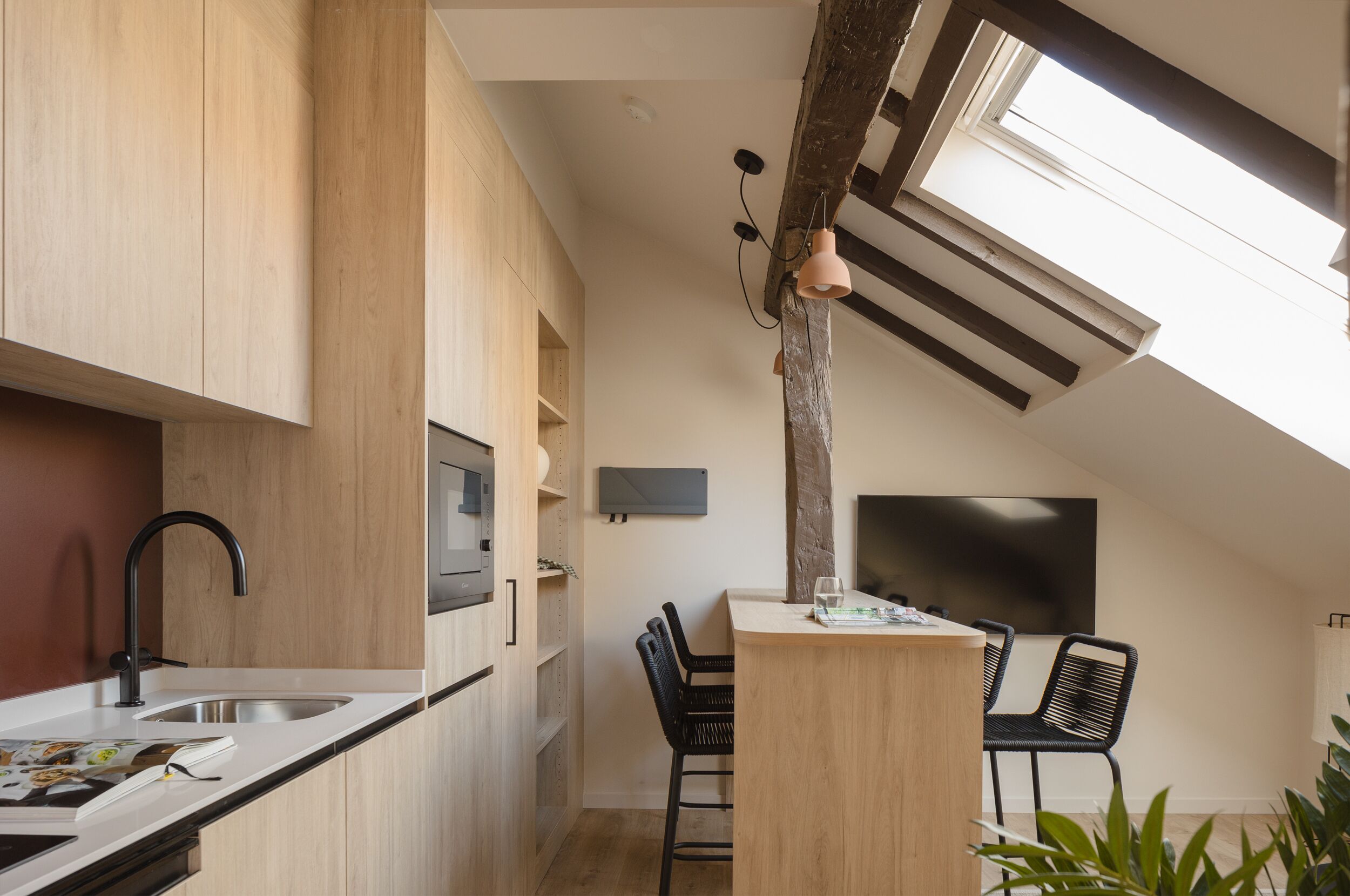 Una cocina moderna con armarios de madera, un grifo negro y un comedor con dos sillas negras y una mesa de madera.