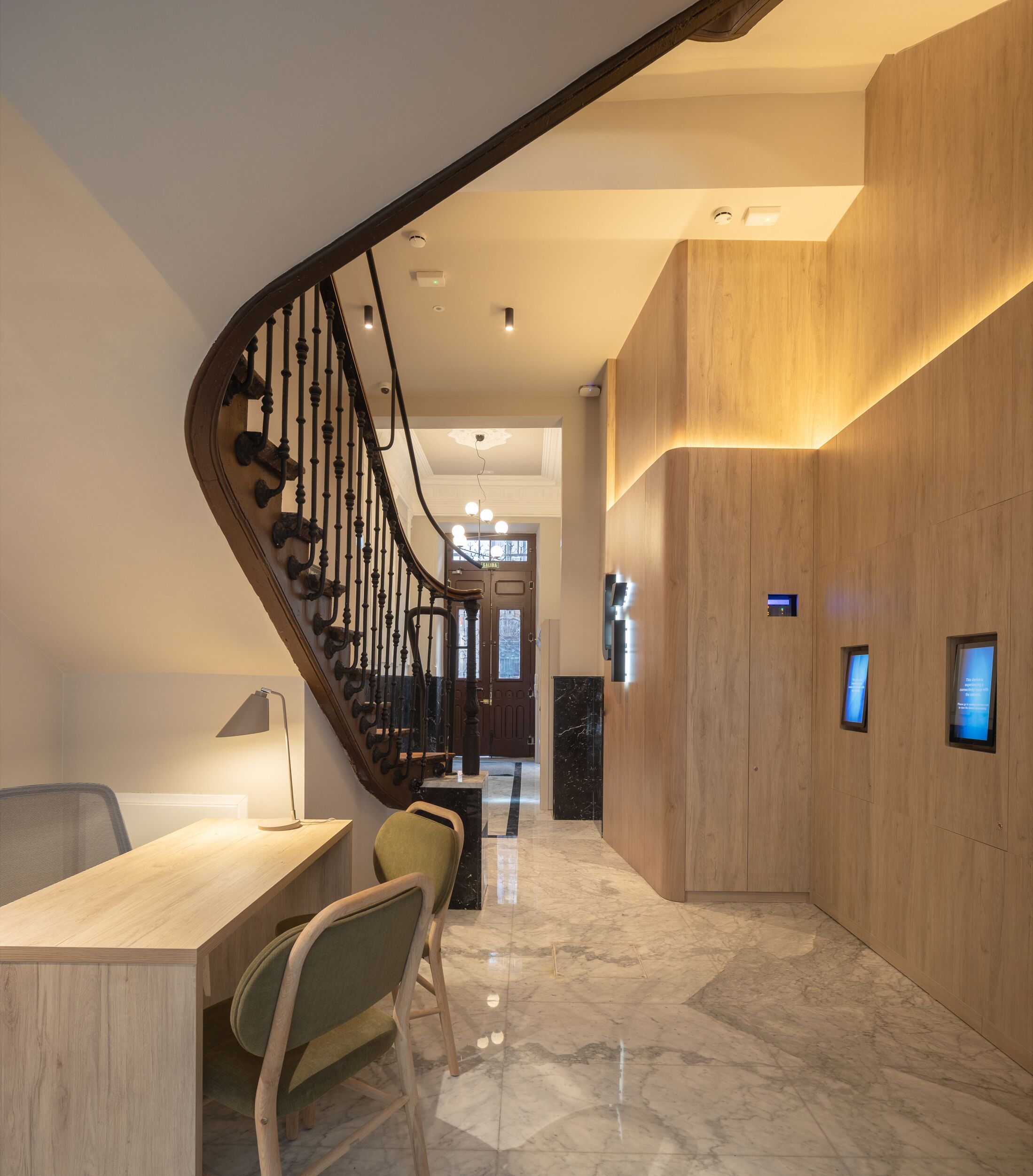 Un interior moderno con una escalera de madera, un mostrador de recepción y un suelo de mármol.
