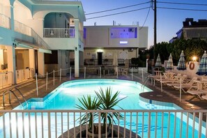 Una piscina con cerca blanca, sillas de descanso y sombrillas.