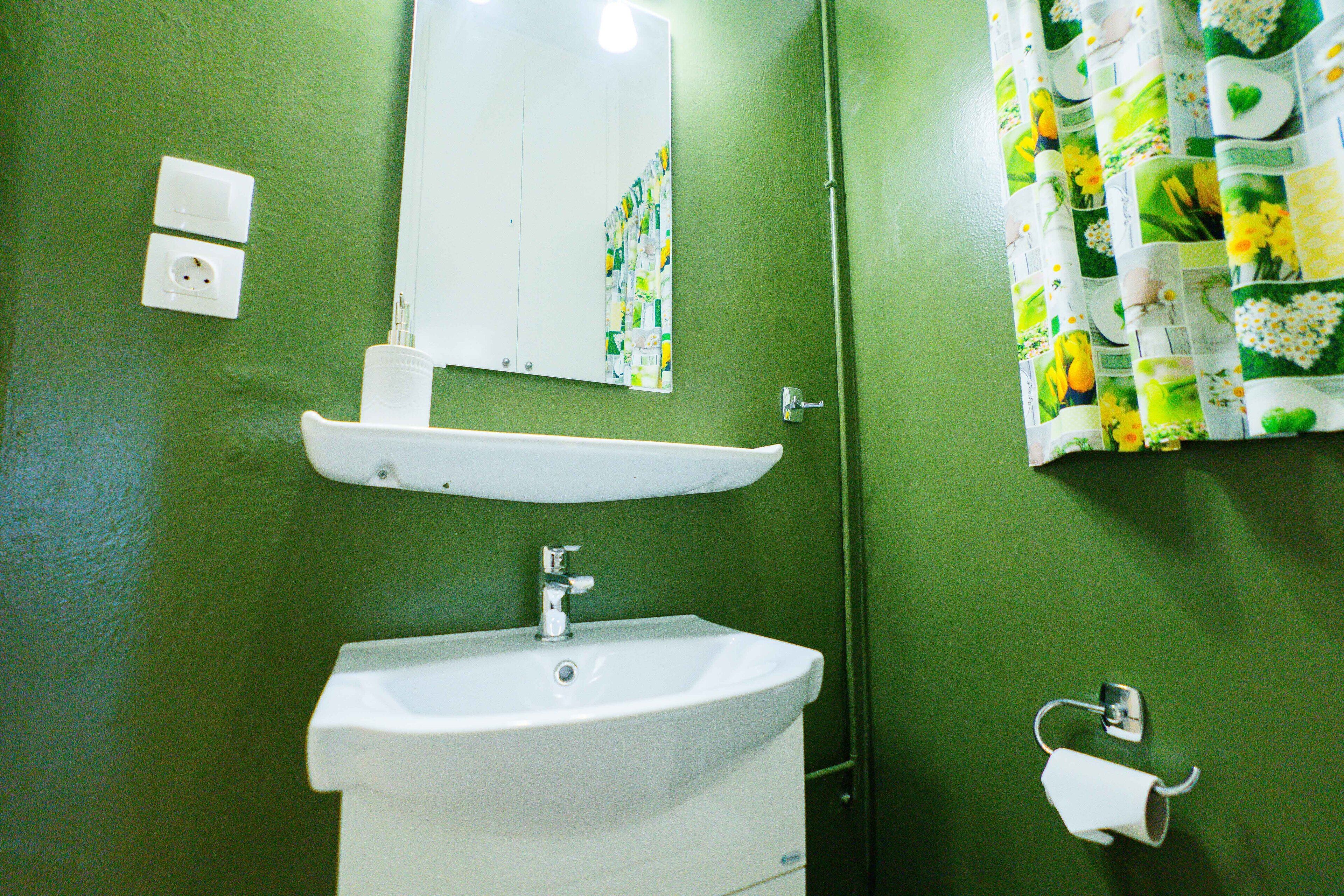 Un baño con lavamanos blanco, un espejo, toallero y dispensador de papel higiénico.