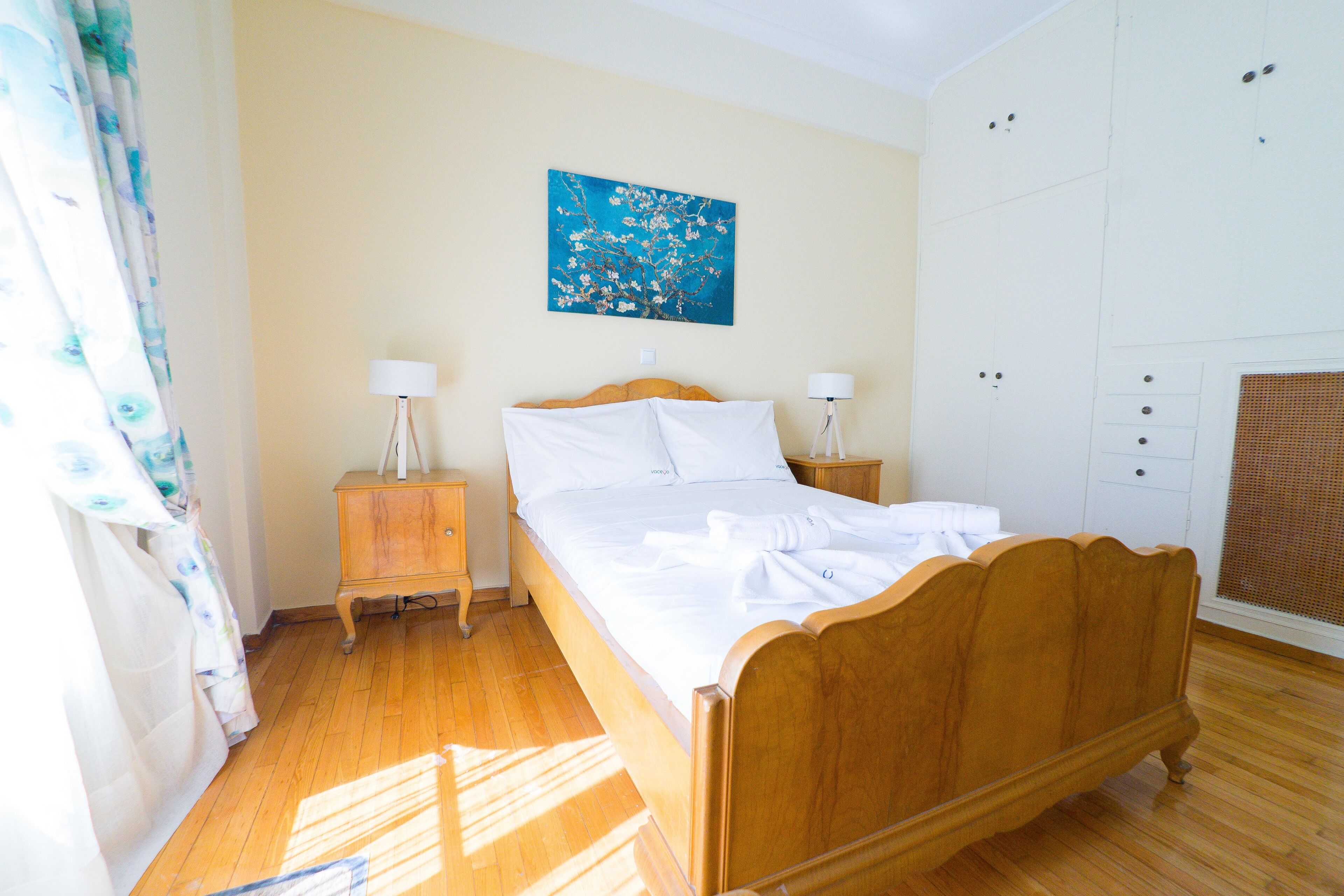 Une chambre à coucher avec un lit en bois, deux tables de chevet avec des lampes, un tableau accroché au mur et une armoire blanche.