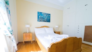 Une chambre à coucher avec un lit en bois, deux tables de chevet avec des lampes, un tableau accroché au mur et une armoire blanche.