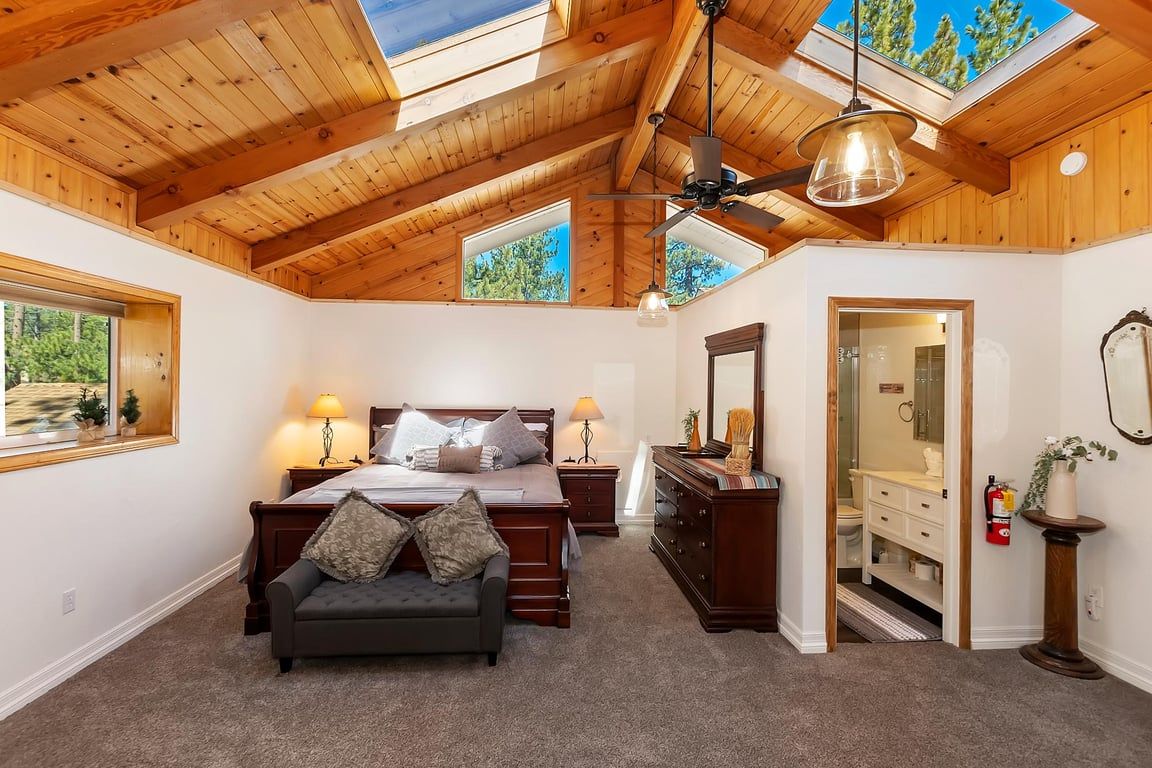 A bedroom with a wooden ceiling, a bed, a dresser, a mirror, and a window.