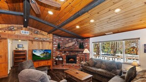 Una sala de estar acogedora con chimenea, techo de madera y un ventanal con vistas a los árboles.