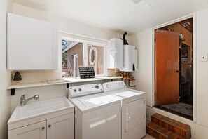 A laundry room with a sink, washing machine, and dryer, a window with a view of the outside, and a wooden door leading to another room. - PET FRIENDLY! Fully Fenced Yard! Close to the Convention Center! 2 Master Suites! (Big Bear City)