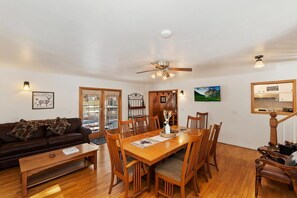 A dining area with a wooden table and chairs, a ceiling fan, and a view of the outdoors through a glass door.