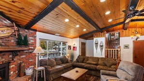 Una sala de estar acogedora con chimenea, vigas de madera en el techo y un amplio ventanal con vistas al exterior.