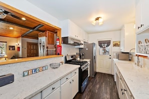 A modern kitchen with white cabinetry, a marble countertop, and a welcome sign.