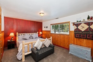 Une chambre à coucher avec un lit en bois, une table de chevet, une commode et une fenêtre donnant sur des arbres.