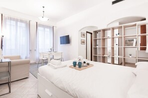 A modern hotel room with a large bed, a desk, a chair, and a bookshelf. - Easylife - Comfort in the Risorgimento area (Milano)