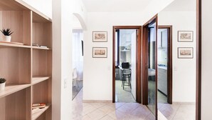 A hallway with wooden shelves, a dining area, and a kitchen visible through an open door.