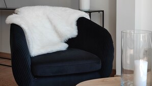 A modern living room with a dark blue armchair, a white throw blanket, pampas grass in a white vase, and a clear glass candle holder. - La Suite Appartement Avec Terrasse Proche Plages Tout a Pied (Concarneau)