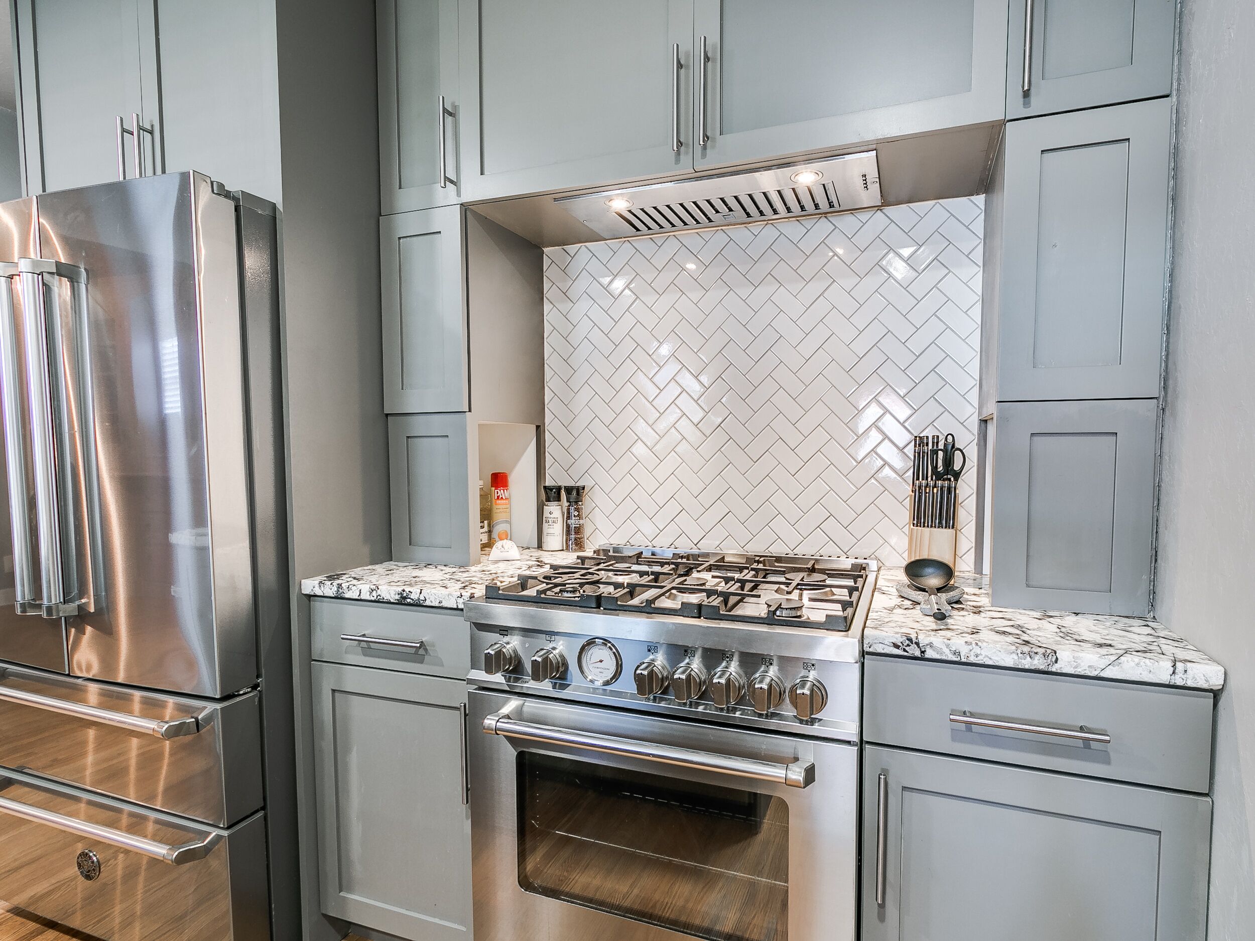 A modern kitchen with stainless steel appliances, a herringbone tile backsplash, and grey cabinetry.