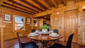 L’intérieur d’un chalet en bois, avec une table à manger ronde, des chaises noires et une plante en pot.