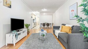 En moderne stue med et fladskærms-tv, en grå sofa og et sofabord i glas.