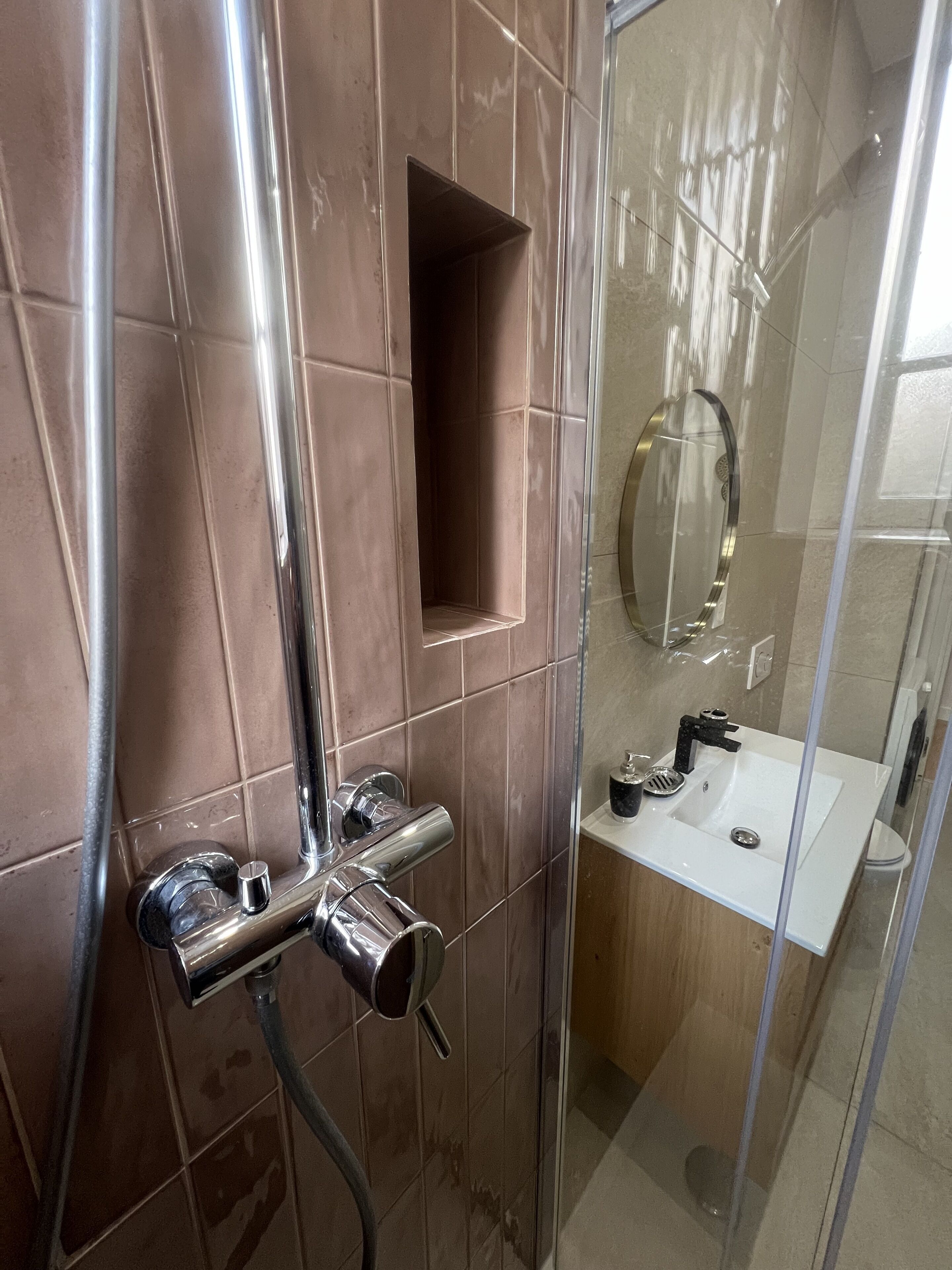 Un baño moderno con ducha de vidrio, grifo cromado y lavamanos blanco con espejo superior.