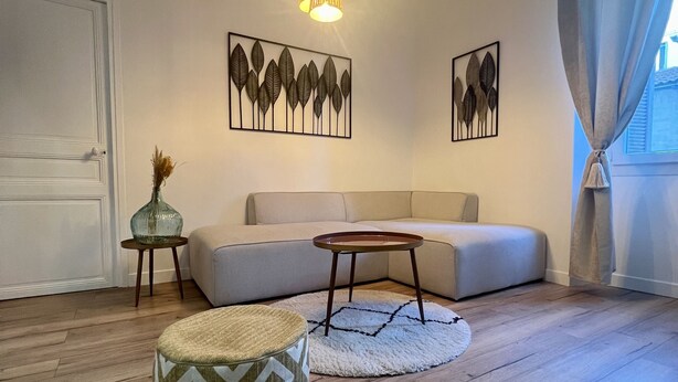 Ein Wohnzimmer mit einer Couch, einem runden Hocker, einem kleinen Beistelltisch und zwei Wandleuchten.