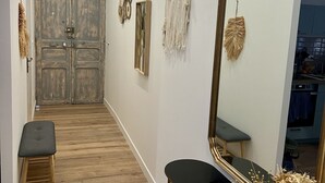 Ein Flur mit Holzboden, einer Bank, einem Spiegel und Wanddekorationen, darunter ein Traumfänger und Wandbilder.