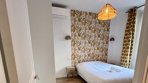 Ein Schlafzimmer mit Holzboden, einem Bett mit weißer Bettwäsche, einer Hängelampe und einer Wand mit Muster.