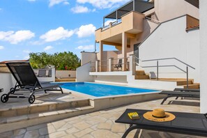 A swimming pool with lounge chairs, a table with a hat, and a staircase leading to a balcony.