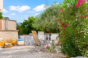 An outdoor seating area with a stone wall, a pool, and a garden with pink flowers. - Apartment Panous 1 with shared Pool in Poreč, Istria (Stranici kod Nove Vasi)