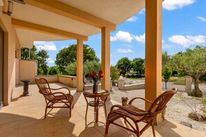 A covered outdoor area with wicker furniture, a table, and a potted plant.