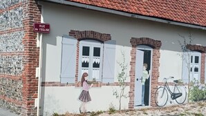 Rakennuksessa on punatiilestä katto, seinässä on suuri seinämaalaus ja siinä on kyltti, jossa lukee: »RUE de l’EGLISE».