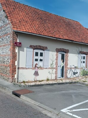 Un edificio con techo de tejas rojas, un mural en la pared y un cartel que dice 'RUE de l'EGLISE'.