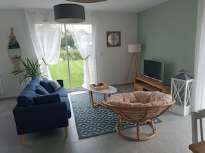 A modern living room with a sofa, a chair, a TV, and a view of a green lawn. - Les Galets -de- Normandie (Petit-Caux)