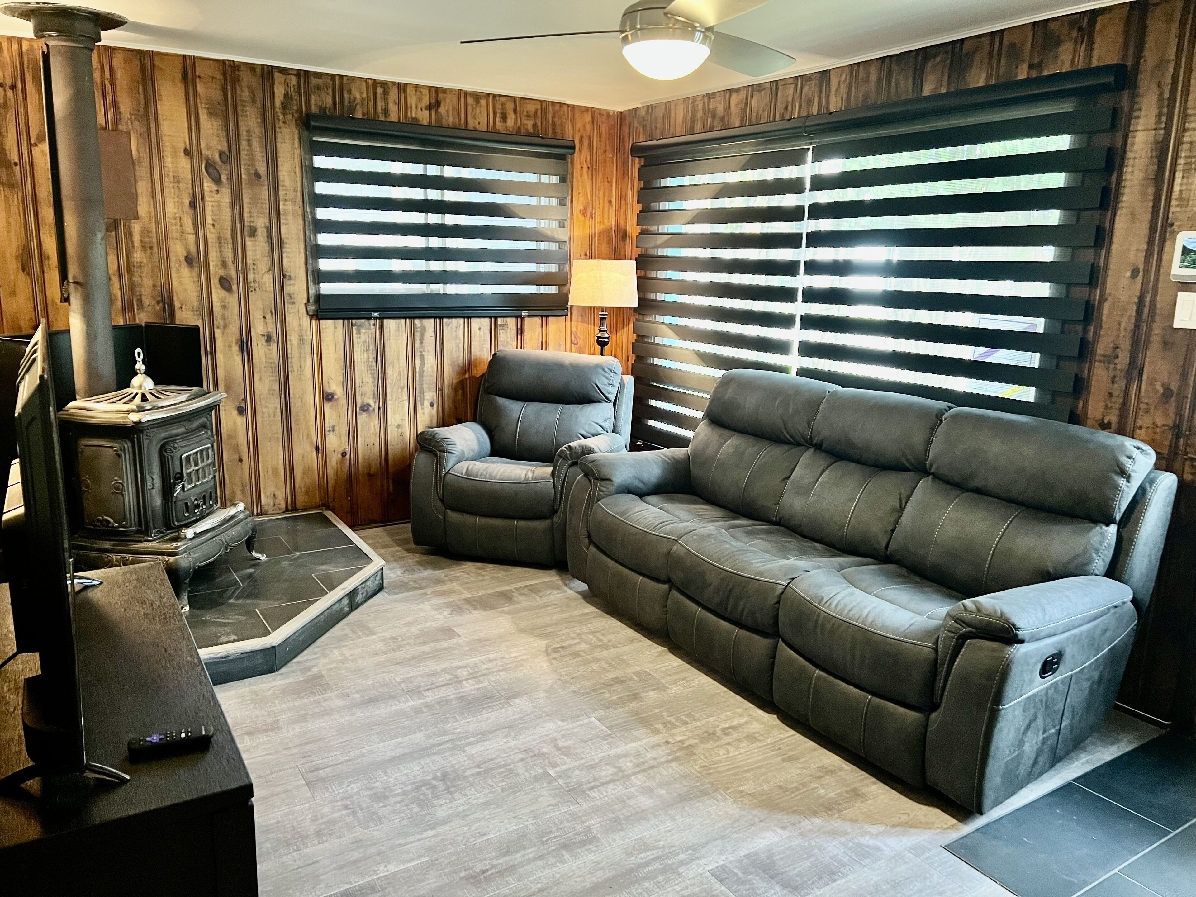 A cozy living room with a sectional sofa, a fireplace, and wooden paneled walls.