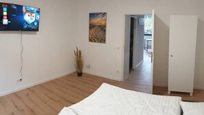 Een slaapkamer met een bed, een aan de muur bevestigde televisie, een schilderij en een deur die naar een andere kamer leidt.